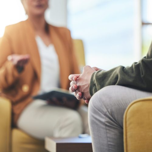 Man, hands and listening for therapy, sofa or advice from woman for mental health, psychology or care. Psychiatrist, patient and frustrated in clinic, session or couch for help, anxiety or depression.